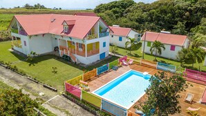 A large house with a swimming pool, surrounded by a colorful fence and palm trees. - Au Jardin Debeauséjour (Capesterre-de-Marie-Galante)
