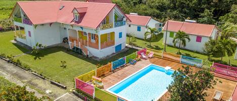 A large house with a swimming pool, surrounded by a colorful fence and palm trees.