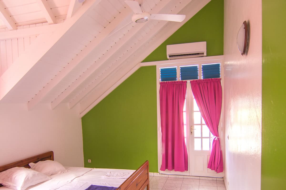 Ein Schlafzimmer mit Bett, Deckenventilator, einer Tür mit Vorhängen und einer grünen Wand.