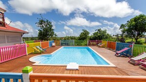 A wooden deck with a swimming pool, colorful fences, and lounge chairs. - Au Jardin Debeauséjour (Capesterre-de-Marie-Galante)