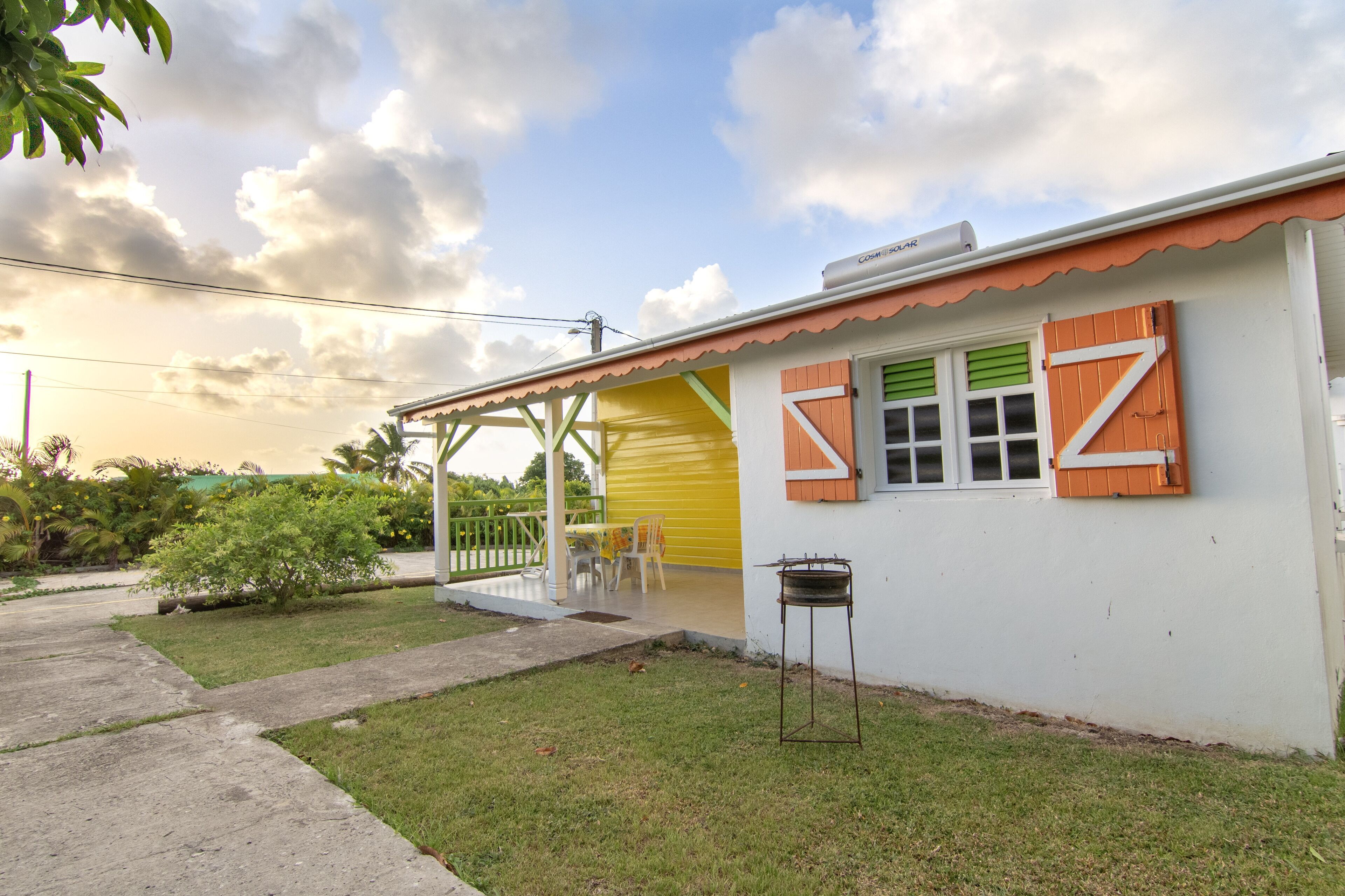 A white building with a yellow door, green shutters, and a covered patio area with chairs.