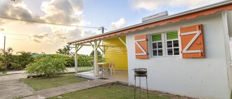 A white building with a yellow door, green shutters, and a covered patio area with chairs.