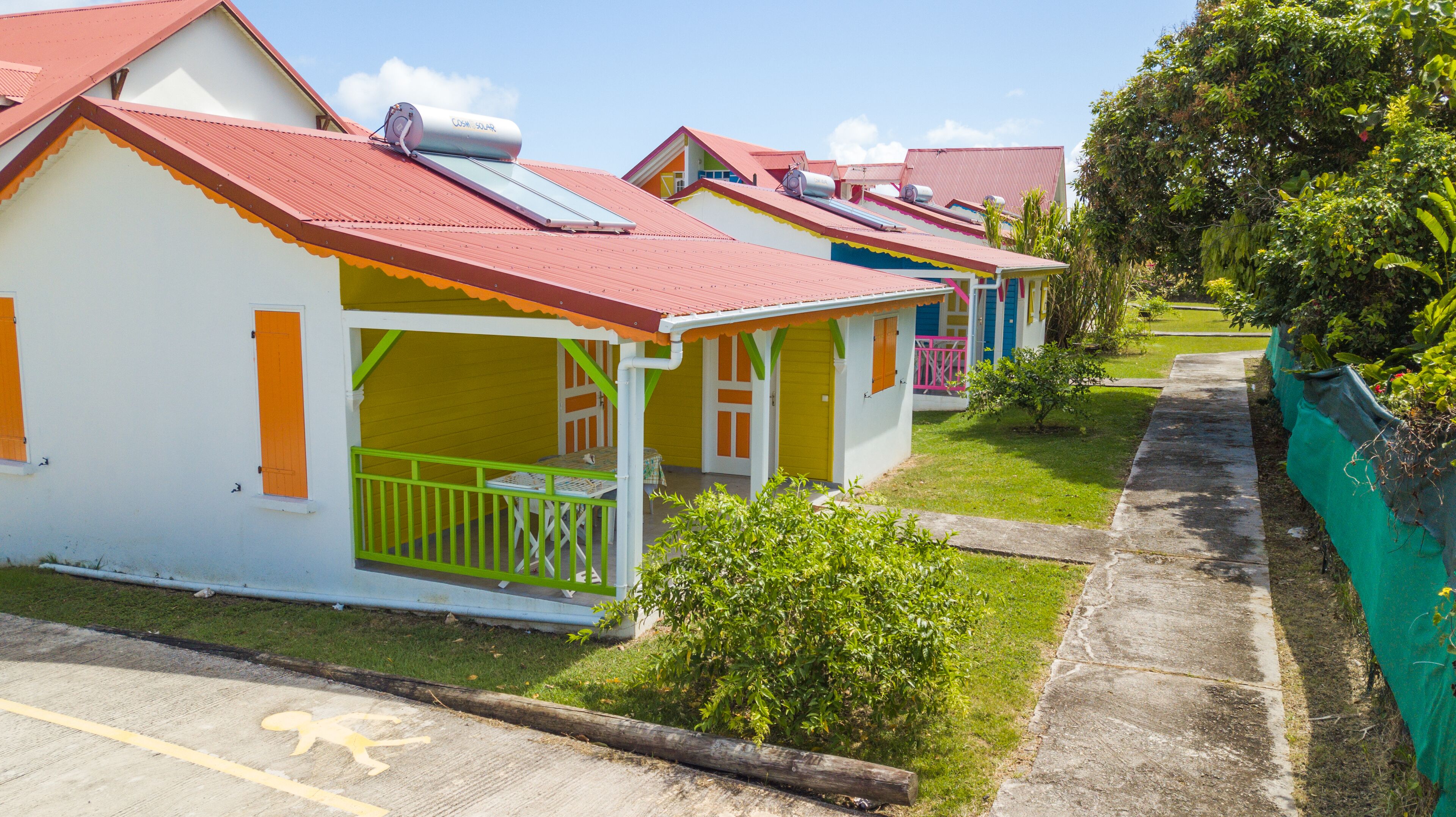 Une rangée de cabanes colorées, de plain-pied, avec des panneaux solaires sur les toits, une petite véranda et un chemin pavé.