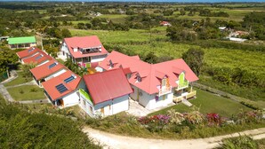 A cluster of houses with red roofs, surrounded by lush greenery and fields. - Au Jardin Debeauséjour (Capesterre-de-Marie-Galante)