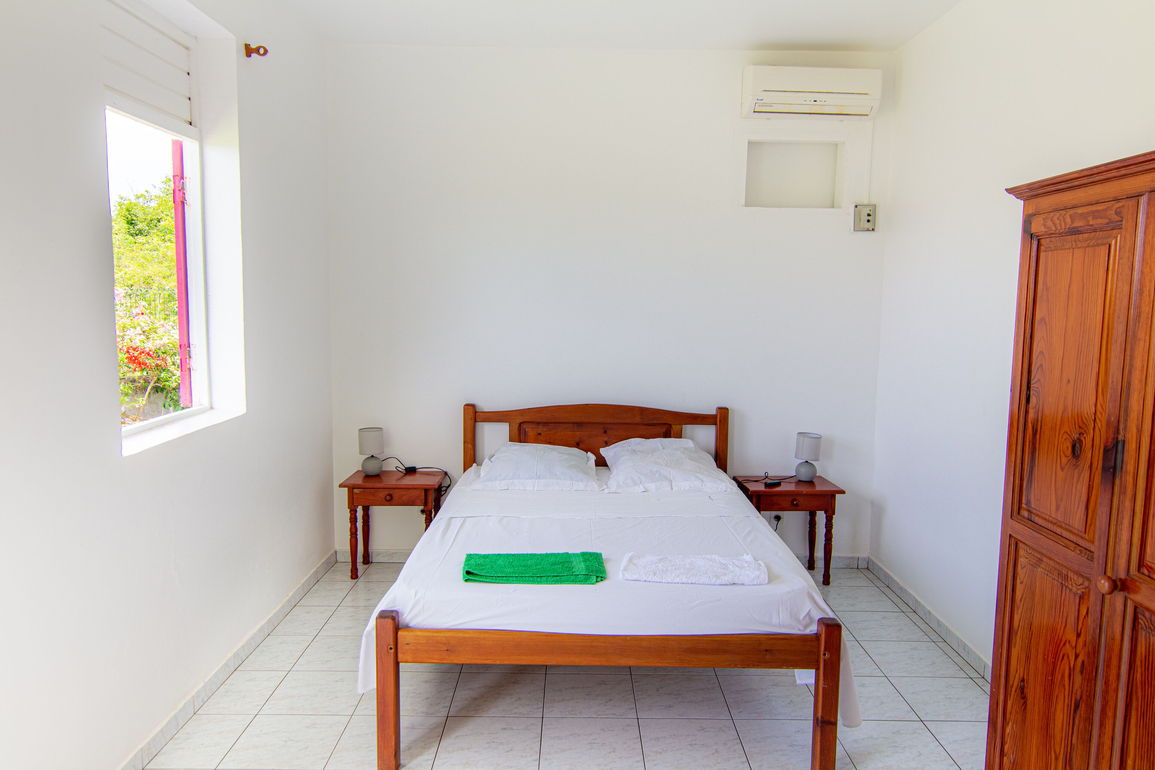 A neatly made bed with a green towel, wooden headboard, and two bedside tables with lamps.