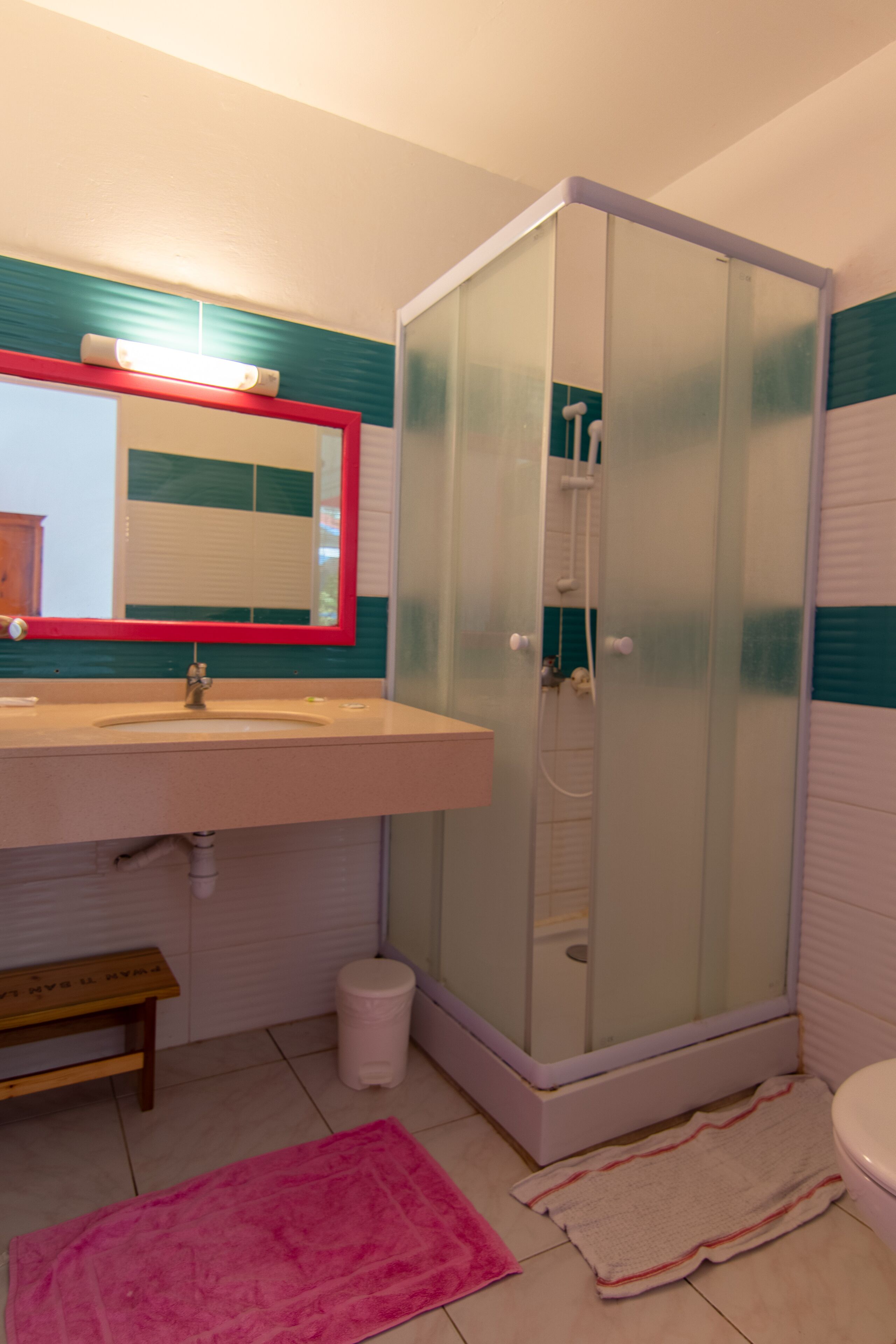 A bathroom with a glass-enclosed shower, a sink with a mirror, and a bench.