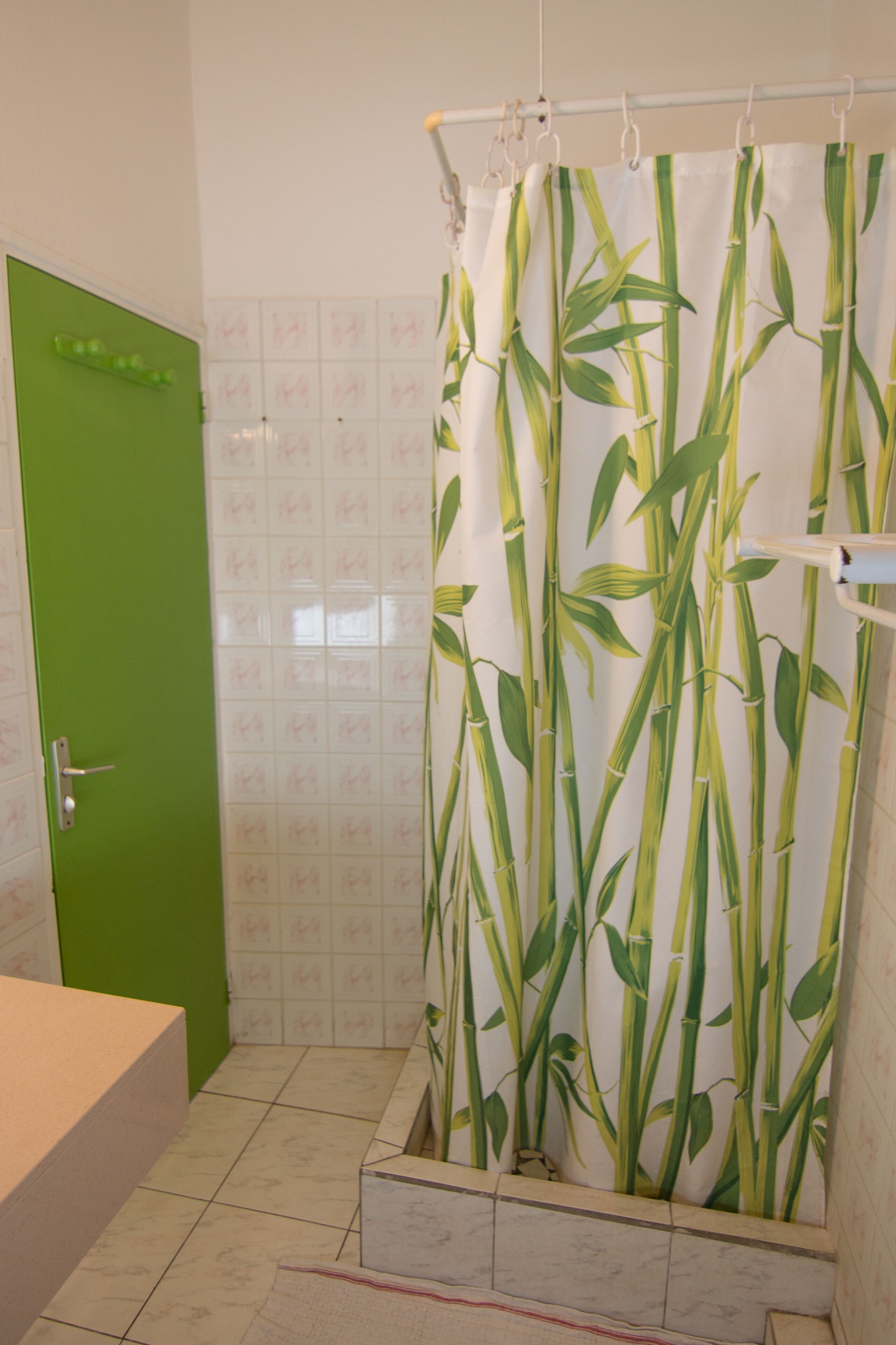 Une salle de bain avec une porte verte, un rideau de douche en bambou et des murs recouverts de carreaux blancs.