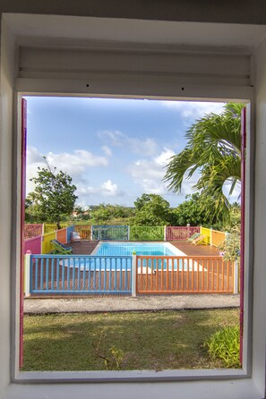 A view of a swimming pool with a wooden deck and colorful fences. - Au Jardin Debeauséjour (Capesterre-de-Marie-Galante)