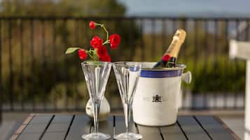 A table with two champagne flutes and a bottle of champagne, a vase with red roses, and a decorative white pot with blue trim.