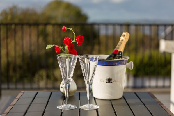 Una mesa con dos copas de champán y una botella, un florero con rosas rojas y una maceta blanca decorada con detalles azules.
