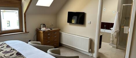 Un dormitorio con cama, cómoda, televisor y vistas al baño.