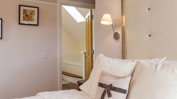 A bedroom with a bed, a nightstand, a wall-mounted lamp, a framed picture, and a door leading to a bathroom.