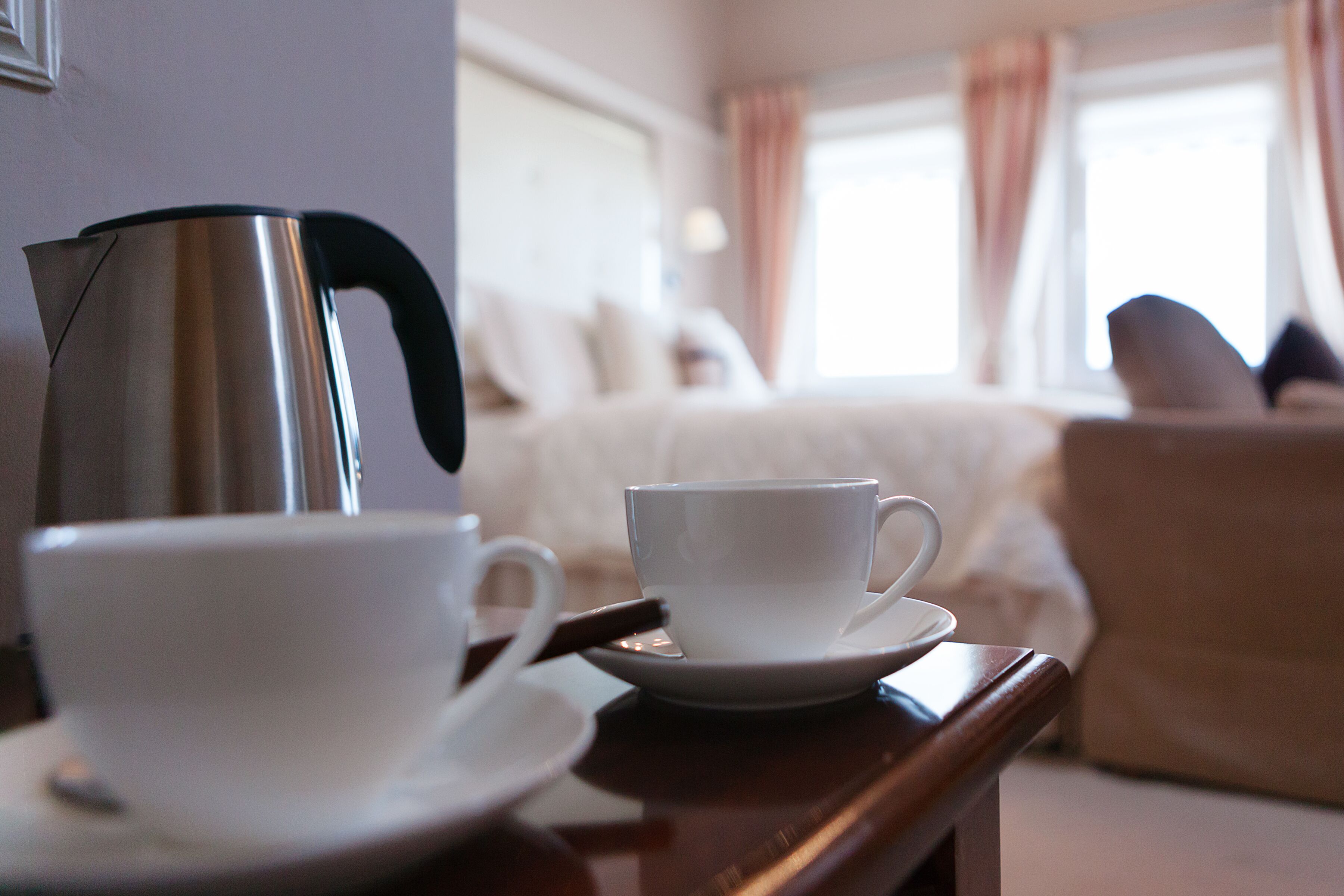 A hotel room with a bed, a coffee maker, and two cups on a tray.