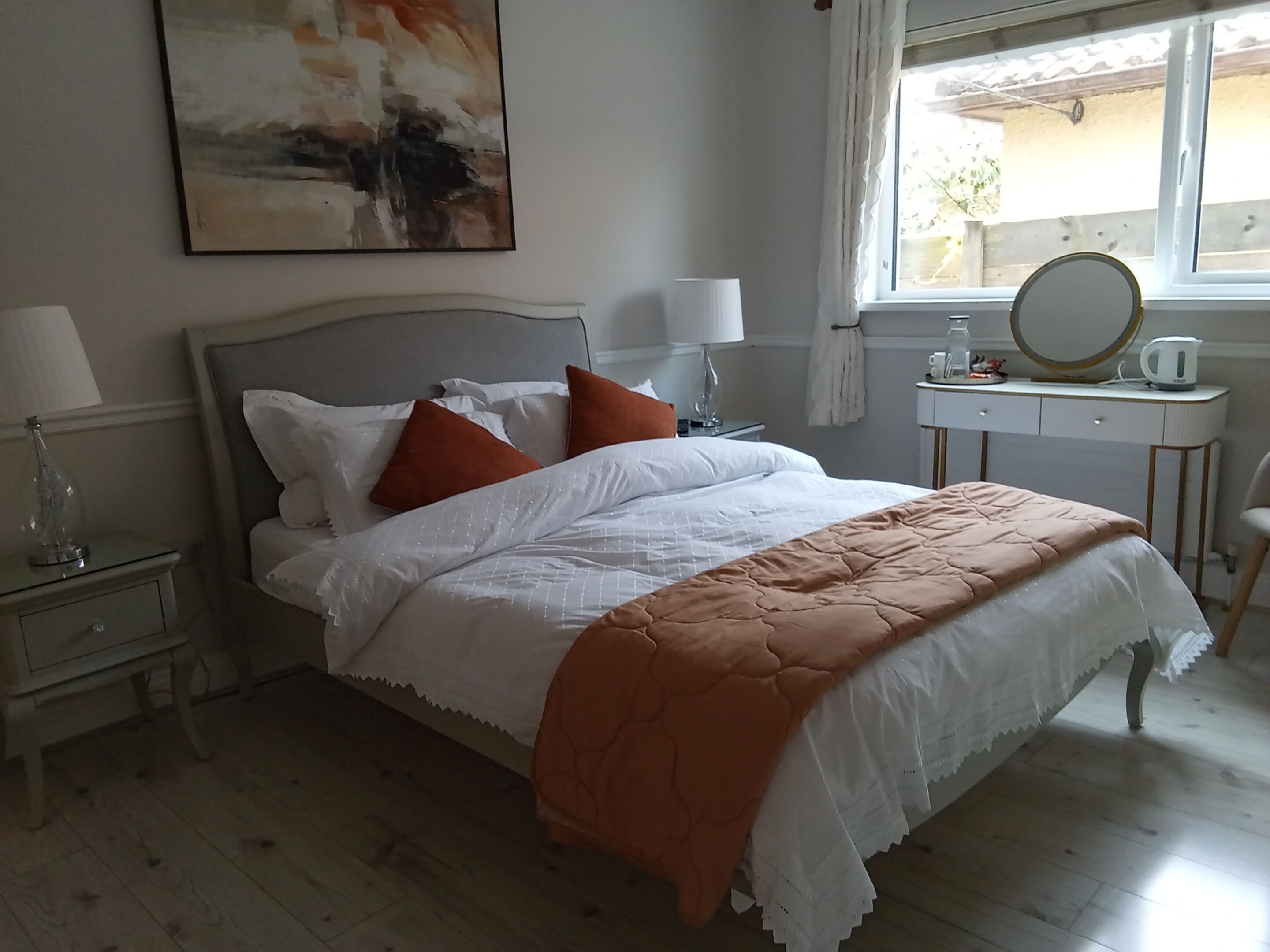 Un lit bien fait, avec des oreillers, une table de chevet avec une lampe, une commode avec un miroir et une fenêtre avec des rideaux.