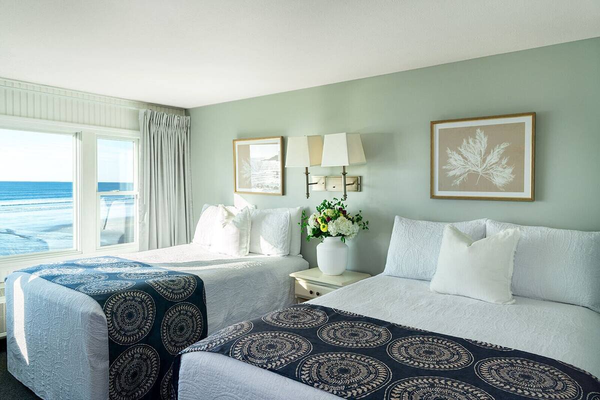 A hotel room with a bed, a chair, a nightstand with a lamp, a vase of flowers, and a framed picture on the wall.
