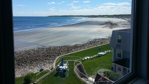 A view of a beach from a window overlooking a grassy area with outdoor seating and a pool. - The Cutty Sark Motel (York Beach)