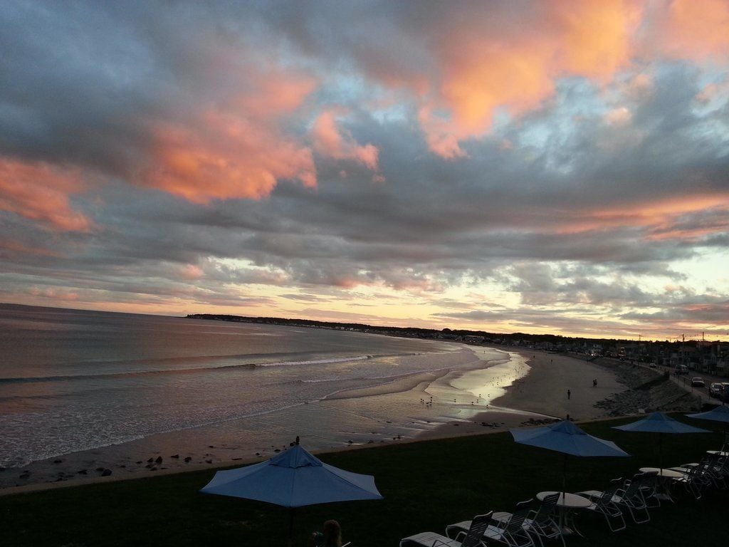 Uma praia com guarda-sóis e cadeiras, vista clara do oceano e céu ao pôr do sol.