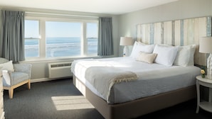 A bedroom with a large bed, a chair, a nightstand, and a view of the ocean. - The Cutty Sark Motel (York Beach)