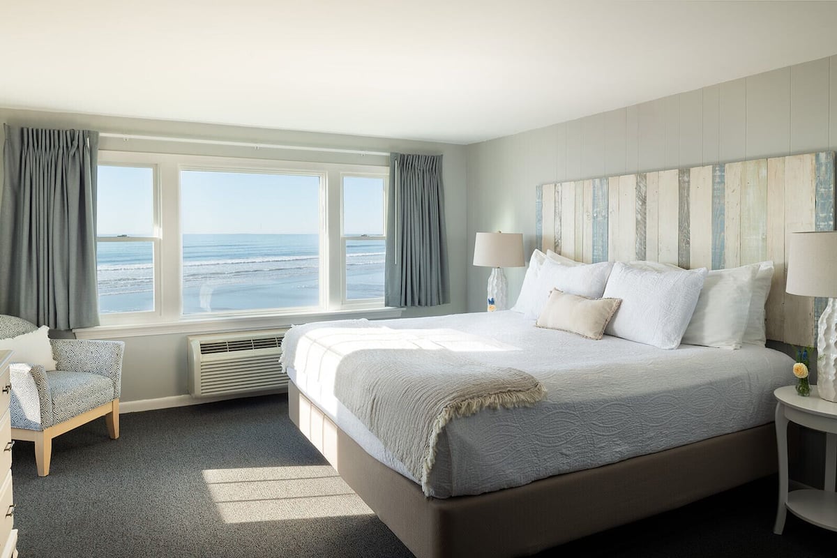 A bedroom with a large bed, a chair, a nightstand, and a view of the ocean.