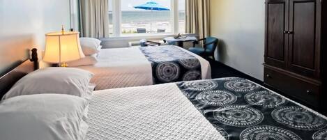 A hotel room with two beds, a desk, a chair, a wardrobe, and a view of the sea through the window.