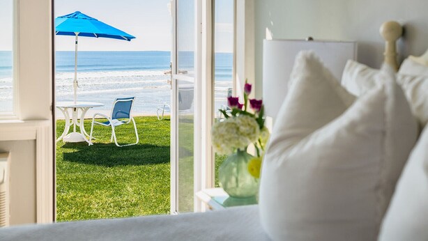 A room with a view of a beach, a blue umbrella, and a white bed with pillows. - The Cutty Sark Motel (York Beach)