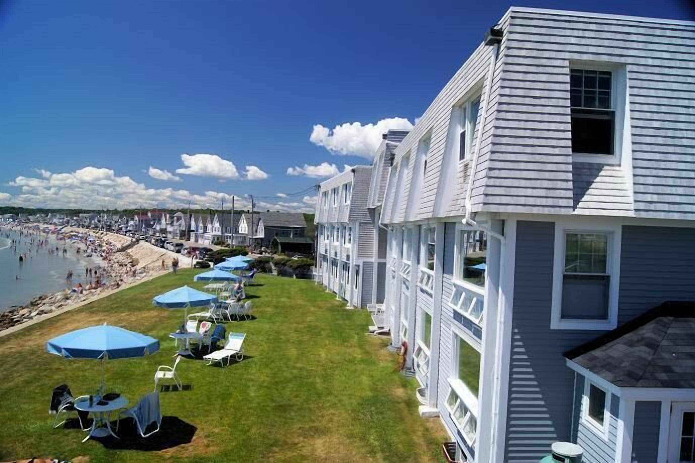 Un hotel frente a la playa con césped, mobiliario exterior y vistas al mar.