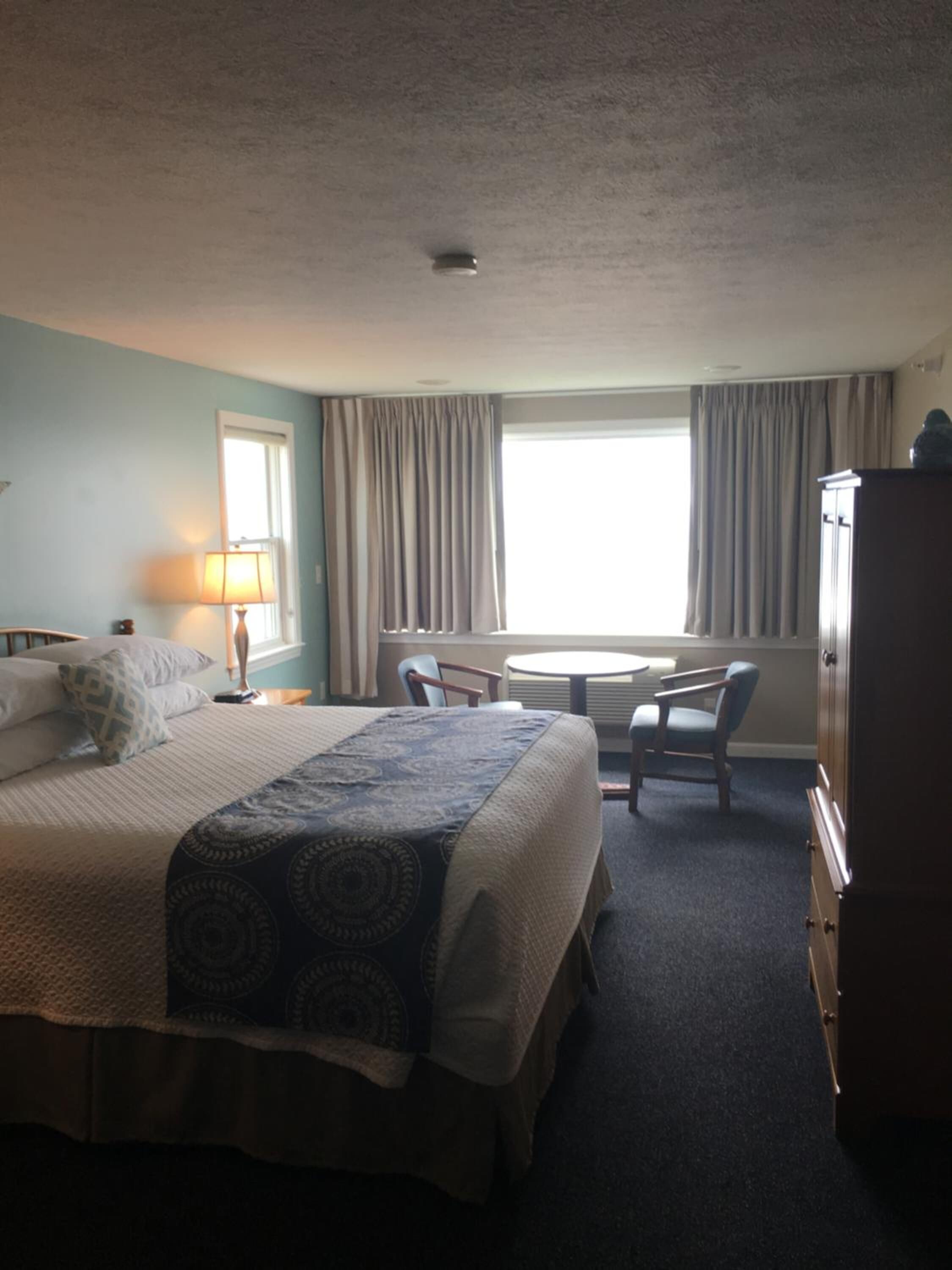 A hotel room with a bed, a desk, two chairs, a lamp, and a wardrobe.
