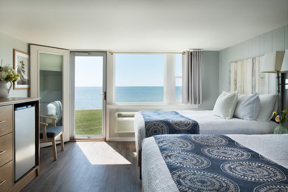 A bedroom with two beds, a desk, and a view of the sea.