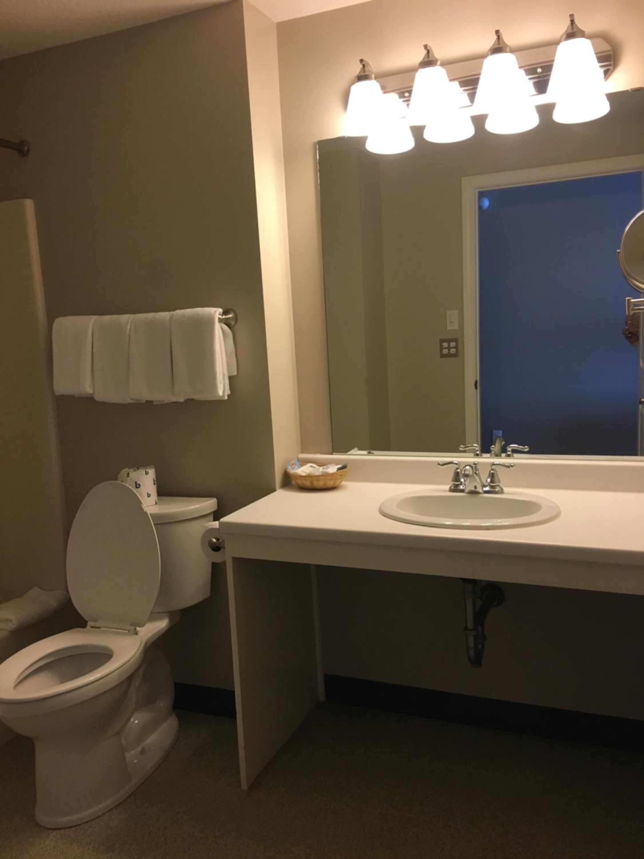A bathroom with a toilet, sink, and mirror. There are towels hanging on the wall.