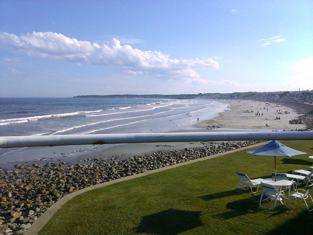 A beach view with a grassy area, chairs, and an umbrella.
