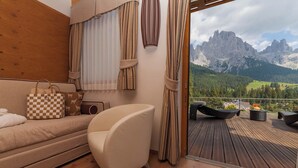 Ein Zimmer mit einer Couch, einem Sessel, einer karierten Tasche und Blick auf Berge vom Balkon aus.