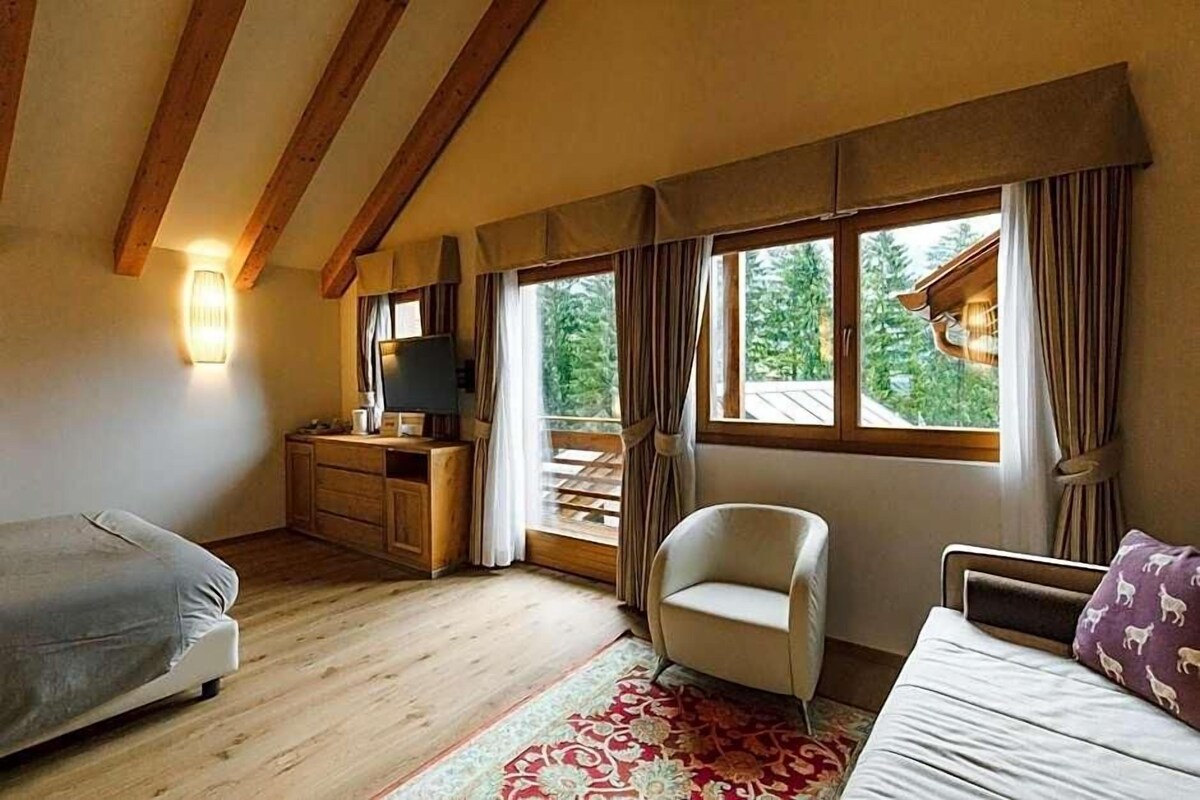Una stanza con un letto, una sedia, una televisione e una finestra con tende.