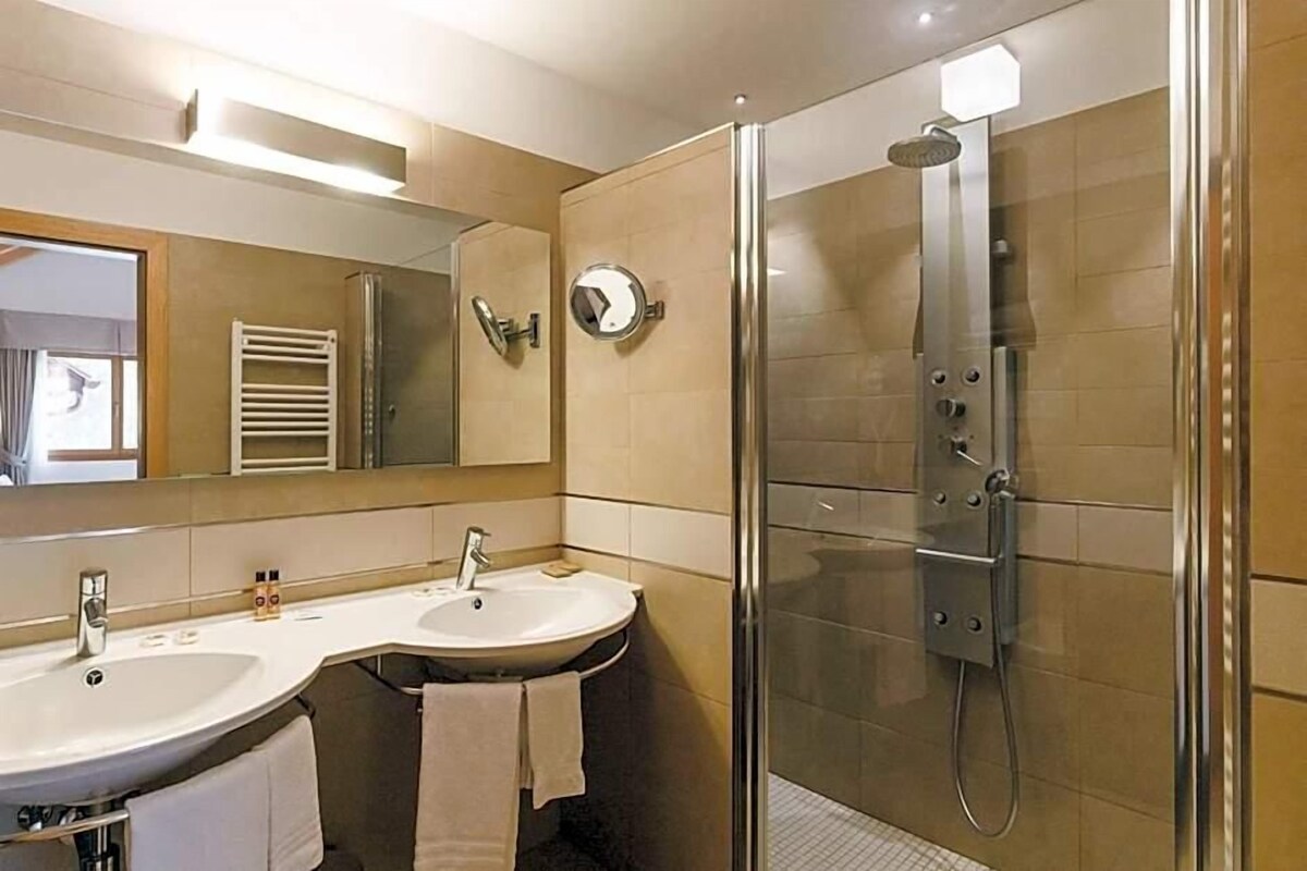 Een moderne badkamer met twee wastafels, een douche met glazen wanden en een grote spiegel.