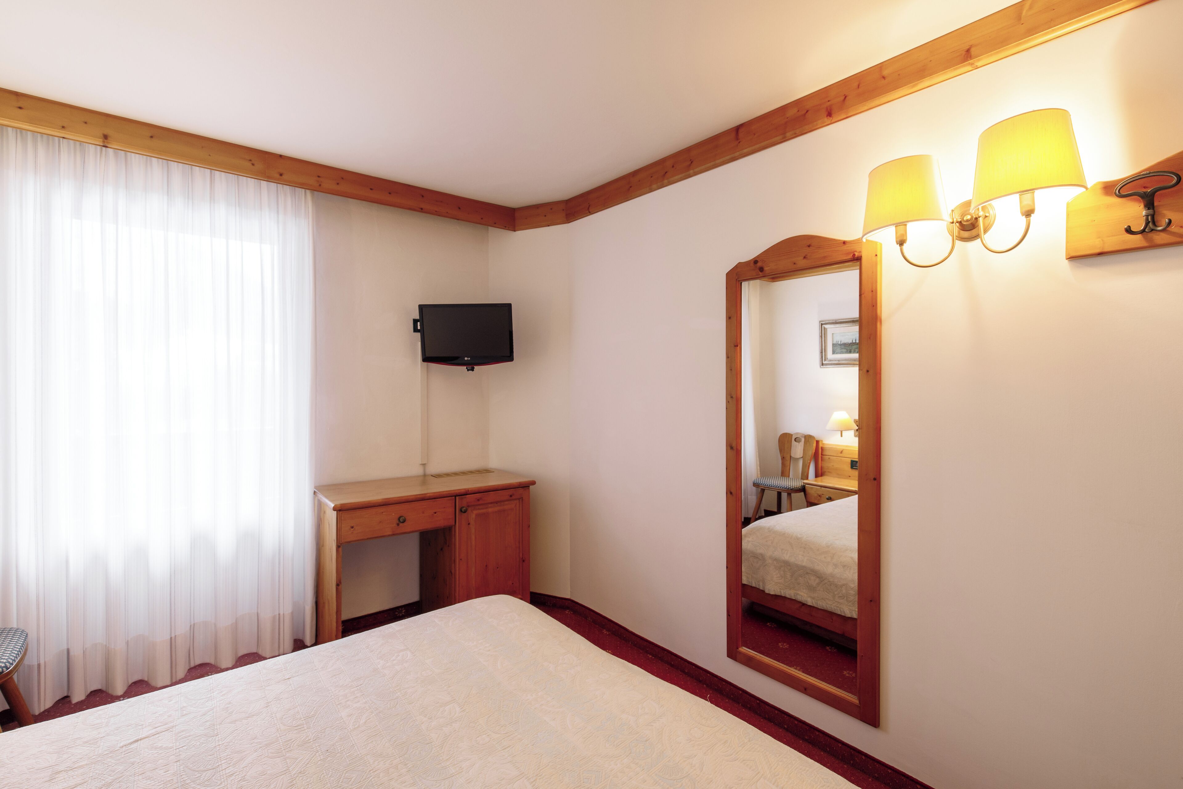 Ein Hotelzimmer mit einem Bett, einem Schreibtisch, einem Sessel, einem Fernseher und einem Spiegel mit Wandleuchten.