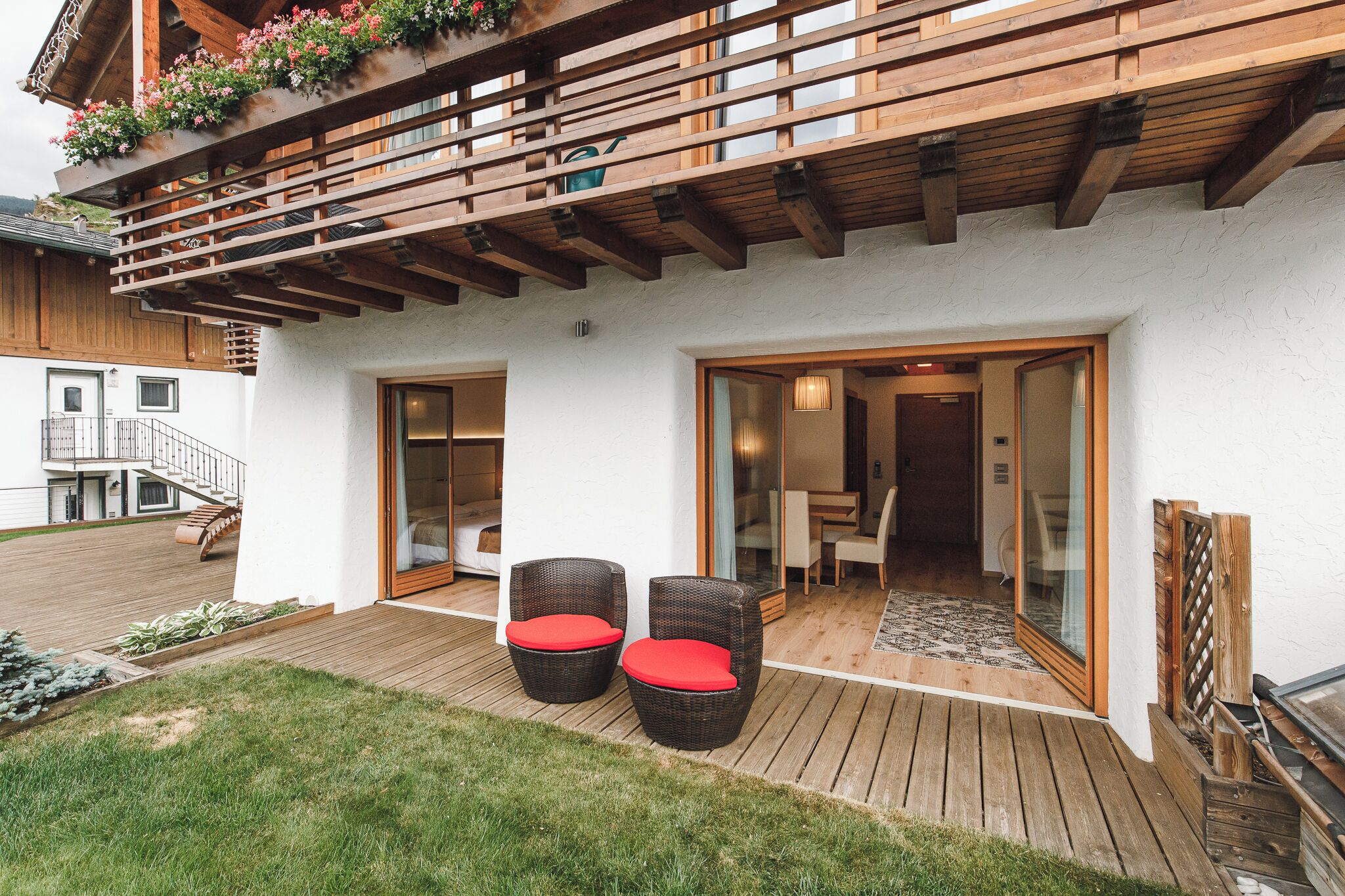 Terraza de madera con sillas de mimbre y una puerta de vidrio que da a un espacio interior.