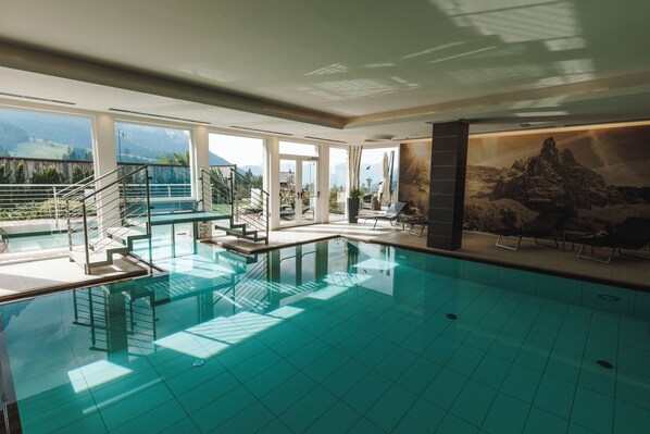 Une grande piscine intérieure avec de larges baies vitrées offrant une vue sur les montagnes.
