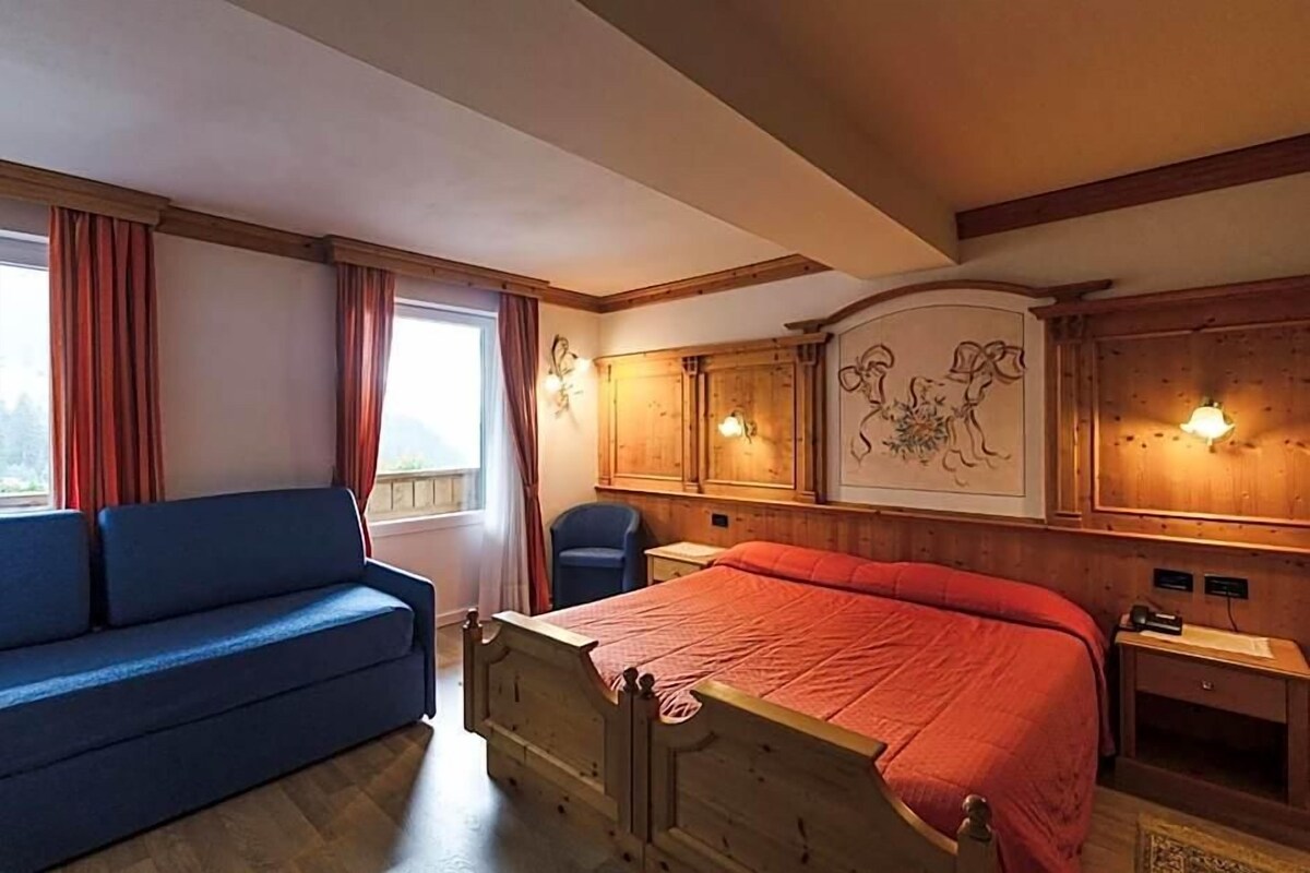 Une chambre à coucher avec un lit en bois, un canapé bleu et une fenêtre avec des rideaux.