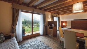 Ein gemütliches Zimmer mit Holzbalkendecke, einer Couch, einem Esstisch und Blick ins Freie.