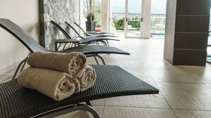 Eine Sitzecke mit zwei Stühlen, jeder mit einem aufgerollten Handtuch. Die Stühle sind schwarz mit einem gewobenen Sitz und Rückenlehne. Der Boden ist mit Fliesen ausgelegt, und im Hintergrund befindet sich eine Steinwand.