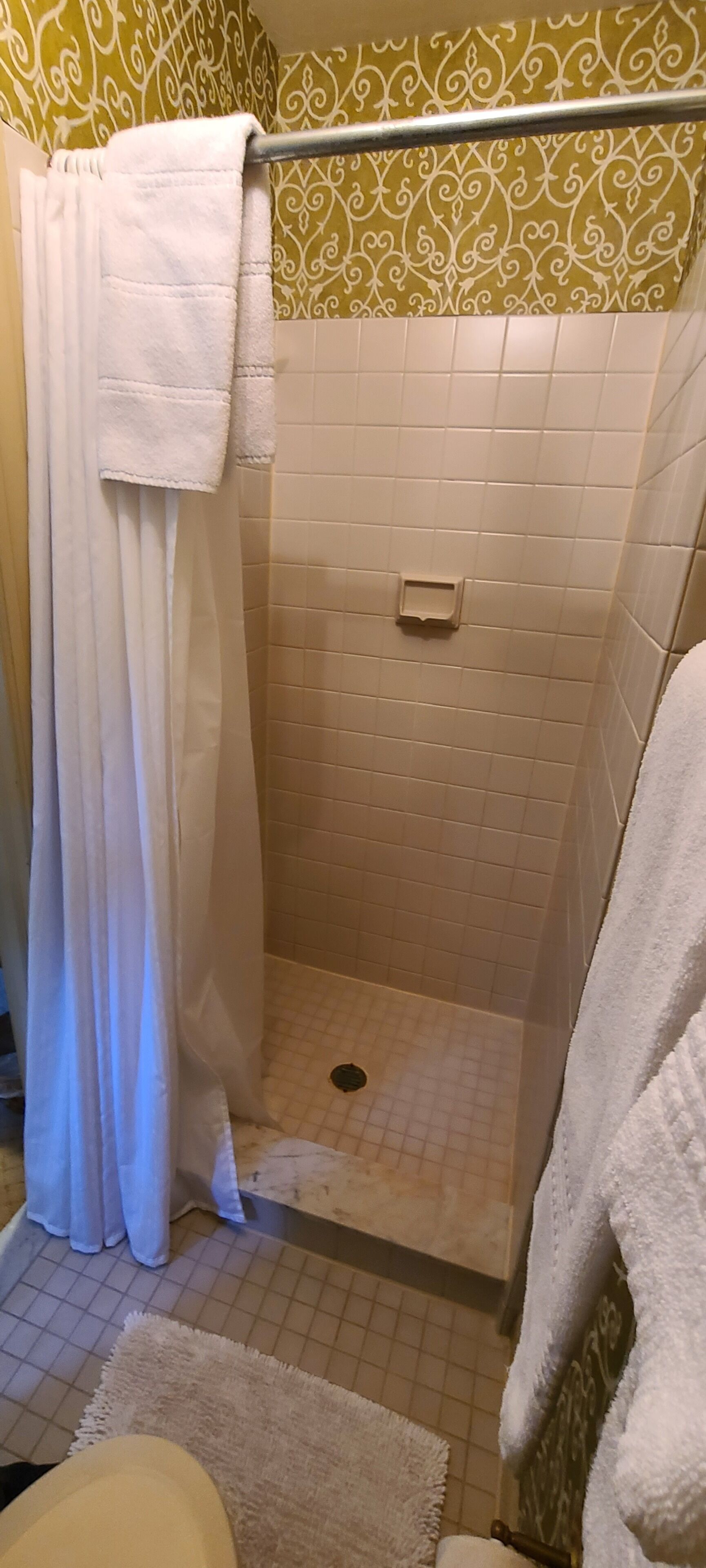 A small, enclosed shower area with a white shower curtain, a white towel hanging on the wall, and a small shelf with a soap dish.