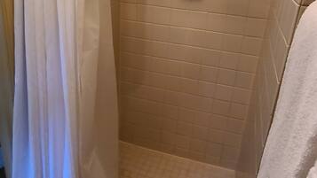 A small, enclosed shower area with a white shower curtain, a white towel hanging on the wall, and a small shelf with a soap dish.