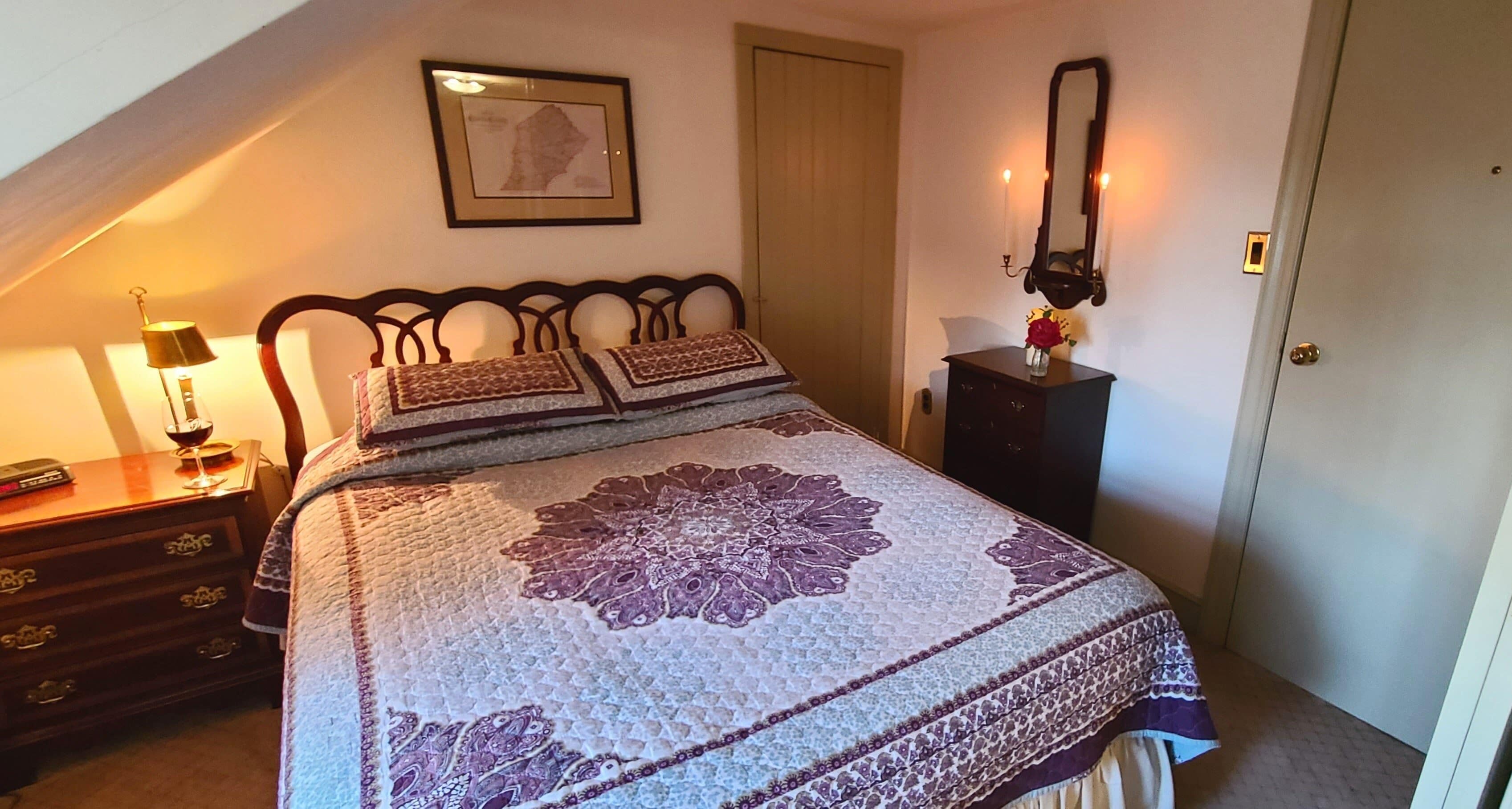 A bedroom with a large bed, a dresser, a nightstand, a mirror, and a framed picture on the wall.