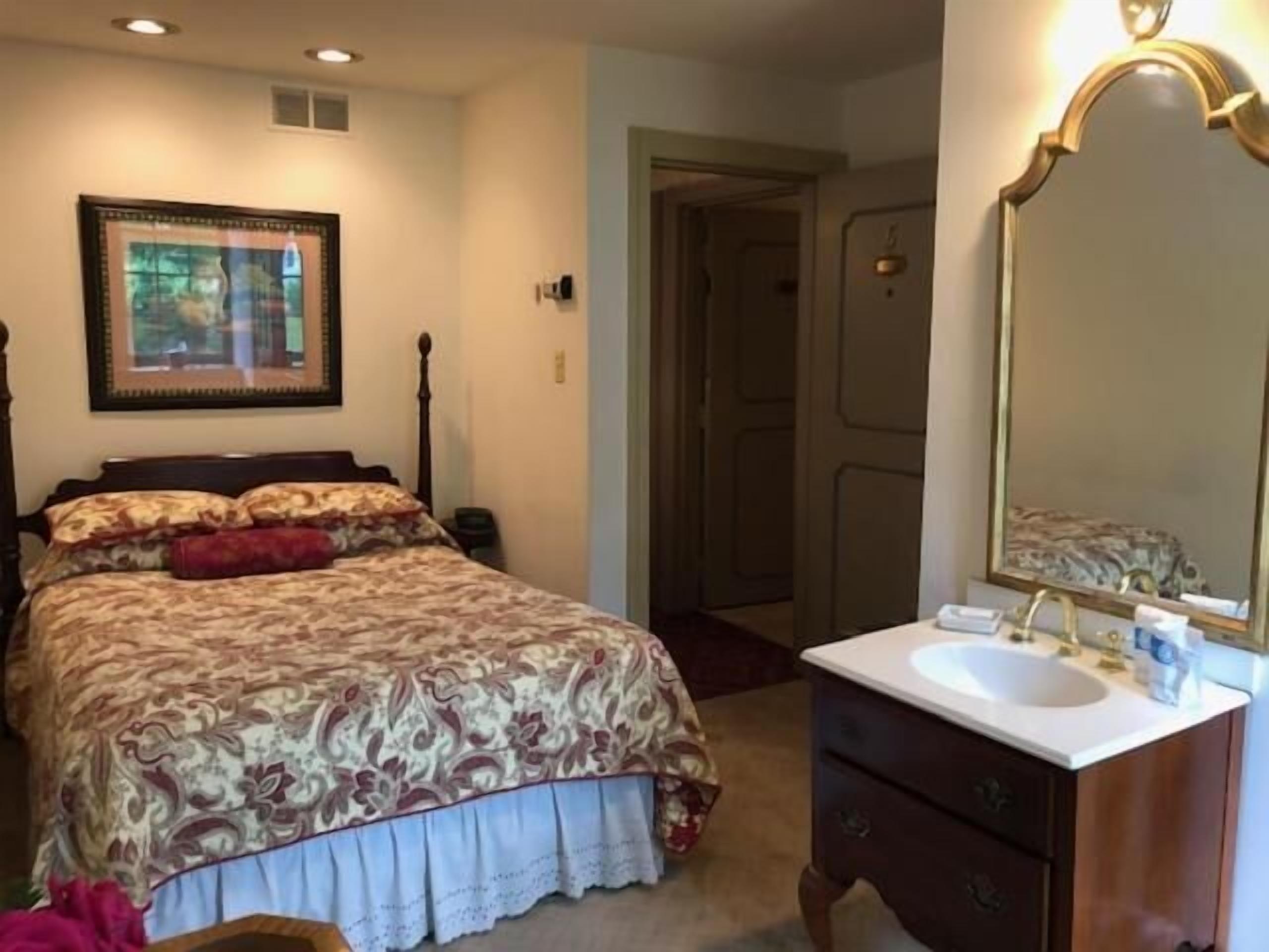 A bedroom with a bed, a bedside table, a dresser, a mirror, and a framed picture on the wall.