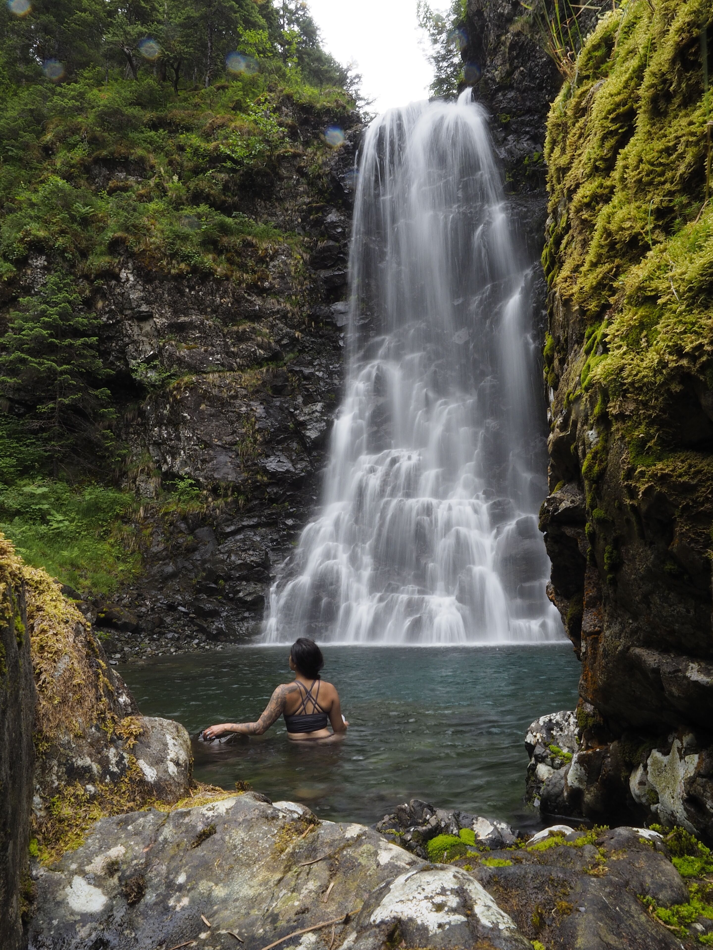 Une cascade dans un environnement naturel, avec une personne assise dans l’eau.
