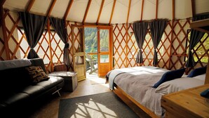 A cozy interior of a yurt with a bed, a sofa, and a wooden table. - Orca Island Cabins (Seward)