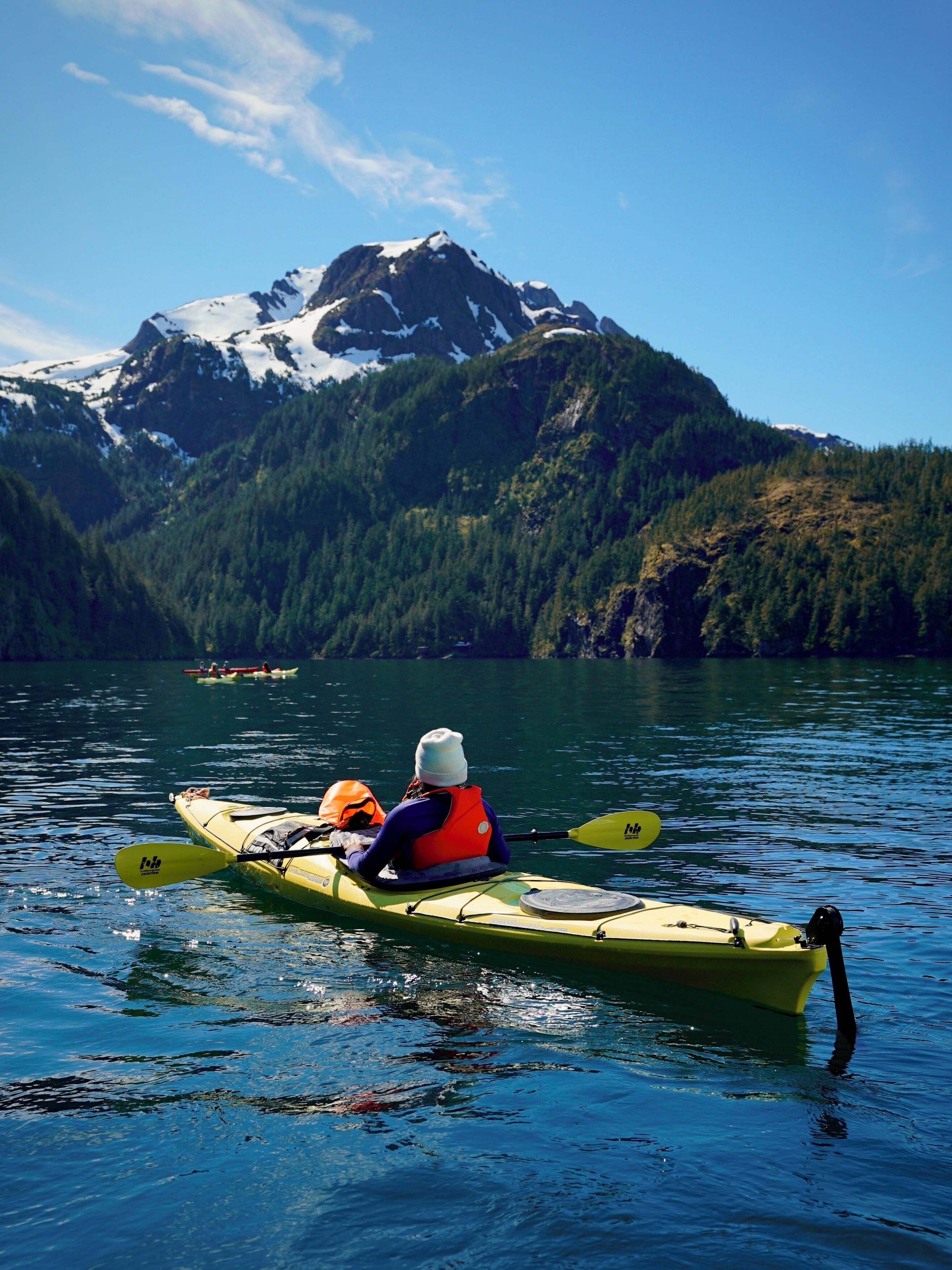 A person kayaking on a calm lake with a mountain in the background.
