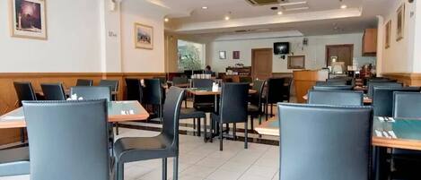 A spacious restaurant with high tables and chairs, a tiled floor, and a television on the wall.