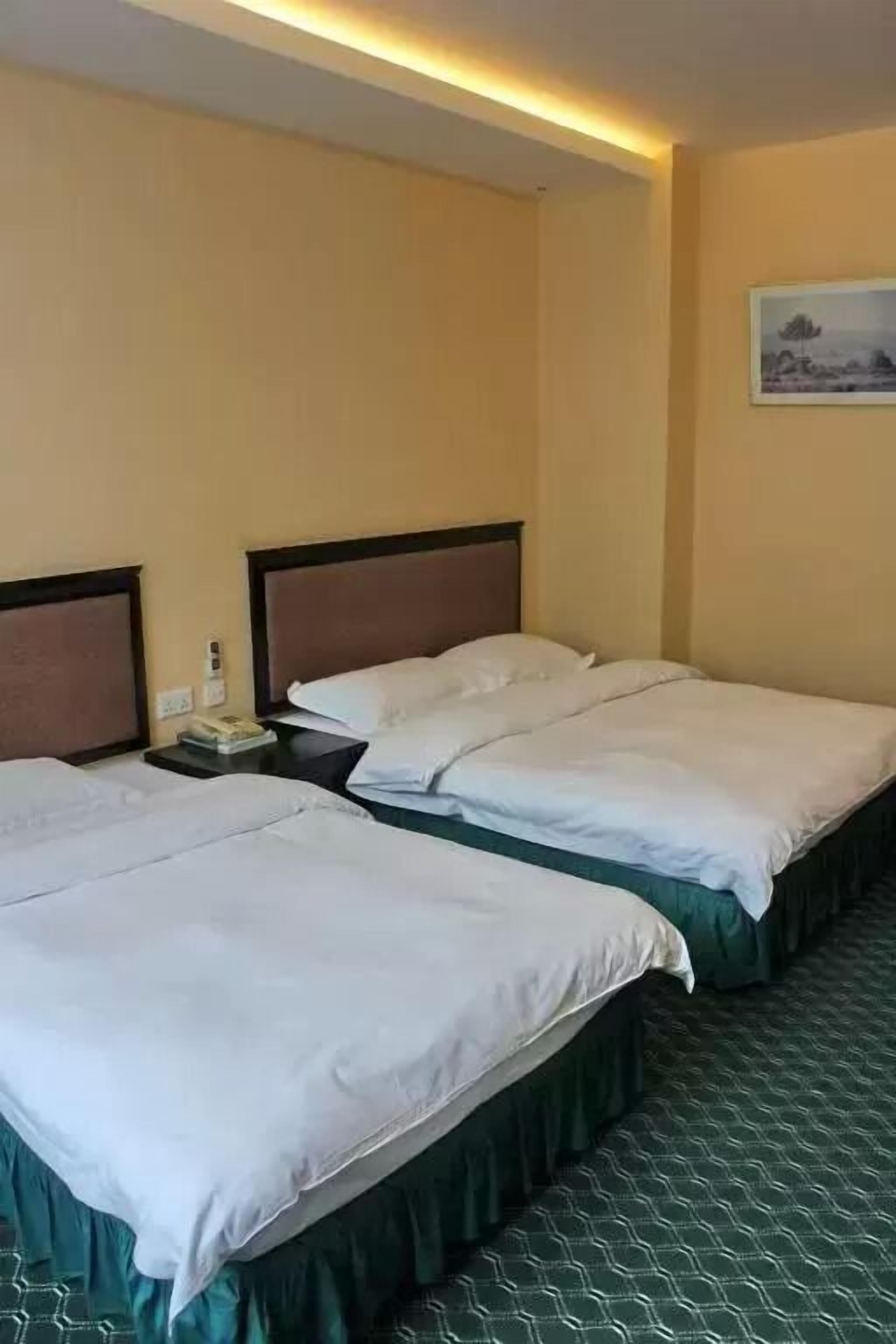 A hotel room with two single beds, a nightstand with a phone and a book, and a painting on the wall.