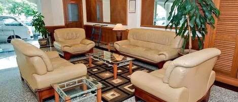 A lobby with three beige sofas, a glass coffee table, and a large potted plant.