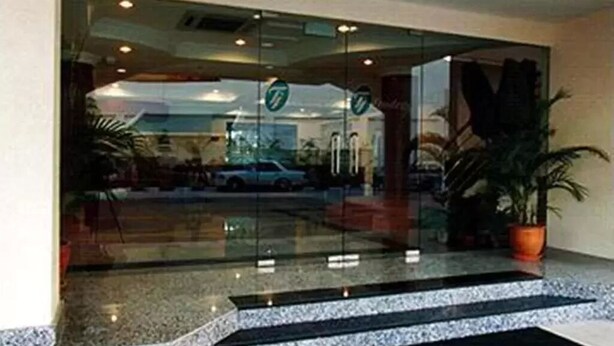 A hotel entrance with a glass door, a potted plant, and a car visible through the window. - Traders Inn (Bandar Seri Begawan)